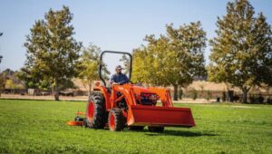 Person driving a Kubota L-series tractor in a field with an attachment mounted to the back.