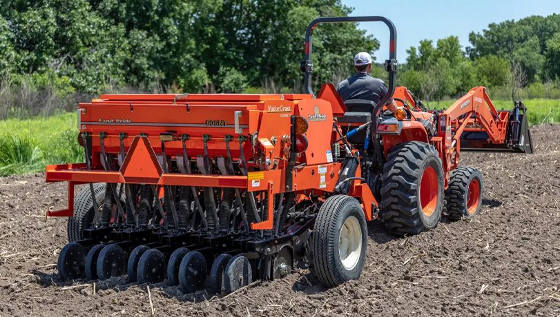 Tractor with a Land Pride 606NT Compact Drill attachment on the back tilling a field.