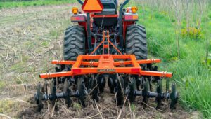 Land Pride DH15 Series Disc Harrows mounted behind a tractor in a field with hay.