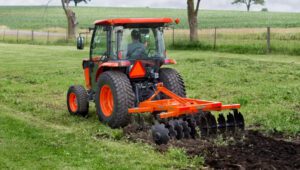 Person driving a tractor with a Land Pride DH25 Series Disc Harrows working a field with a fence in the background.