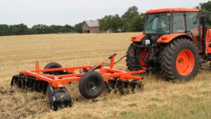 New Land Pride DH35 Series Disc Harrows attached to a Kubota tractor working in a field with hay.