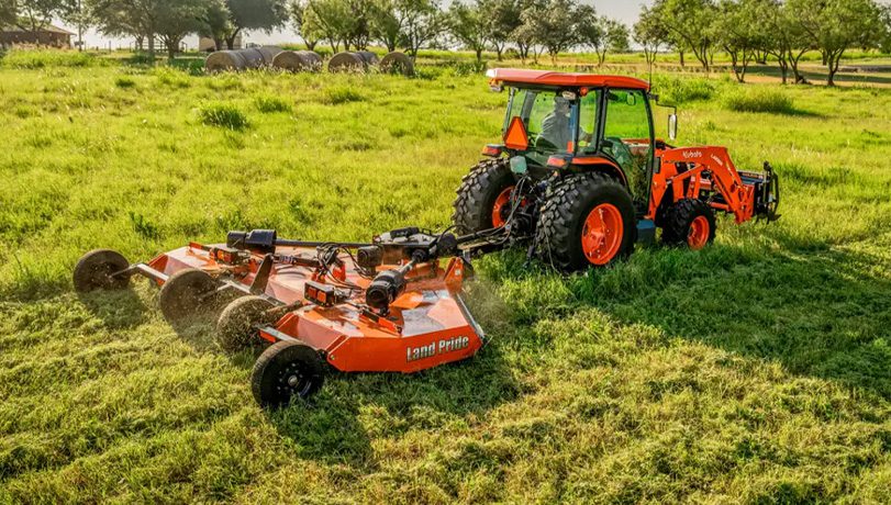 New Land Pride RC2512 Rotary Cutters attached to the back of a Kubota tractor cutting grass in an overgrown pasture.