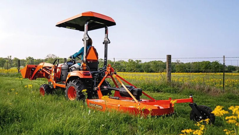 Person driving a Kubota tractor with a Land Pride RCR12 Series Rotary Cutter attachment on the back.