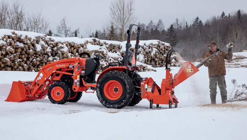 Worker using a Land Pride WC1503 Wood Chipper attached to a Kubota tractor grinding down a tree branch.