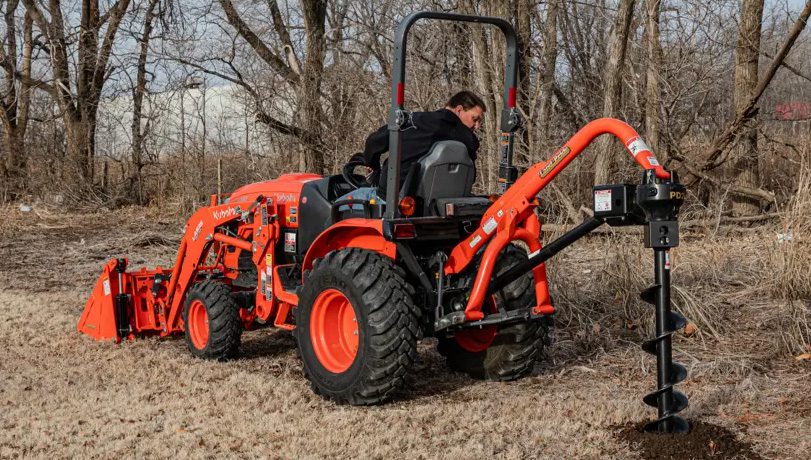 Land Pride PD25 Series Post Hole Digger mounted on a Kubota tractor near some trees.