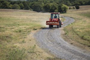 Kubota tractor with an excavator attachment driving down a gravel road.