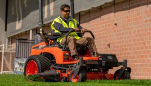 Landscaping professional driving a Kubota ZD1021-60 Mower around a large building.