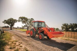Person driving a Kubota L-Series tractor down a gravel road with a Land Pride attachment on the back.