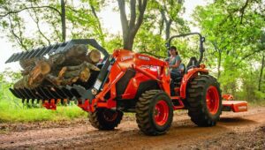 Person on a Kubota tractor driving down a dirt trail clearing land with specialized attachments.