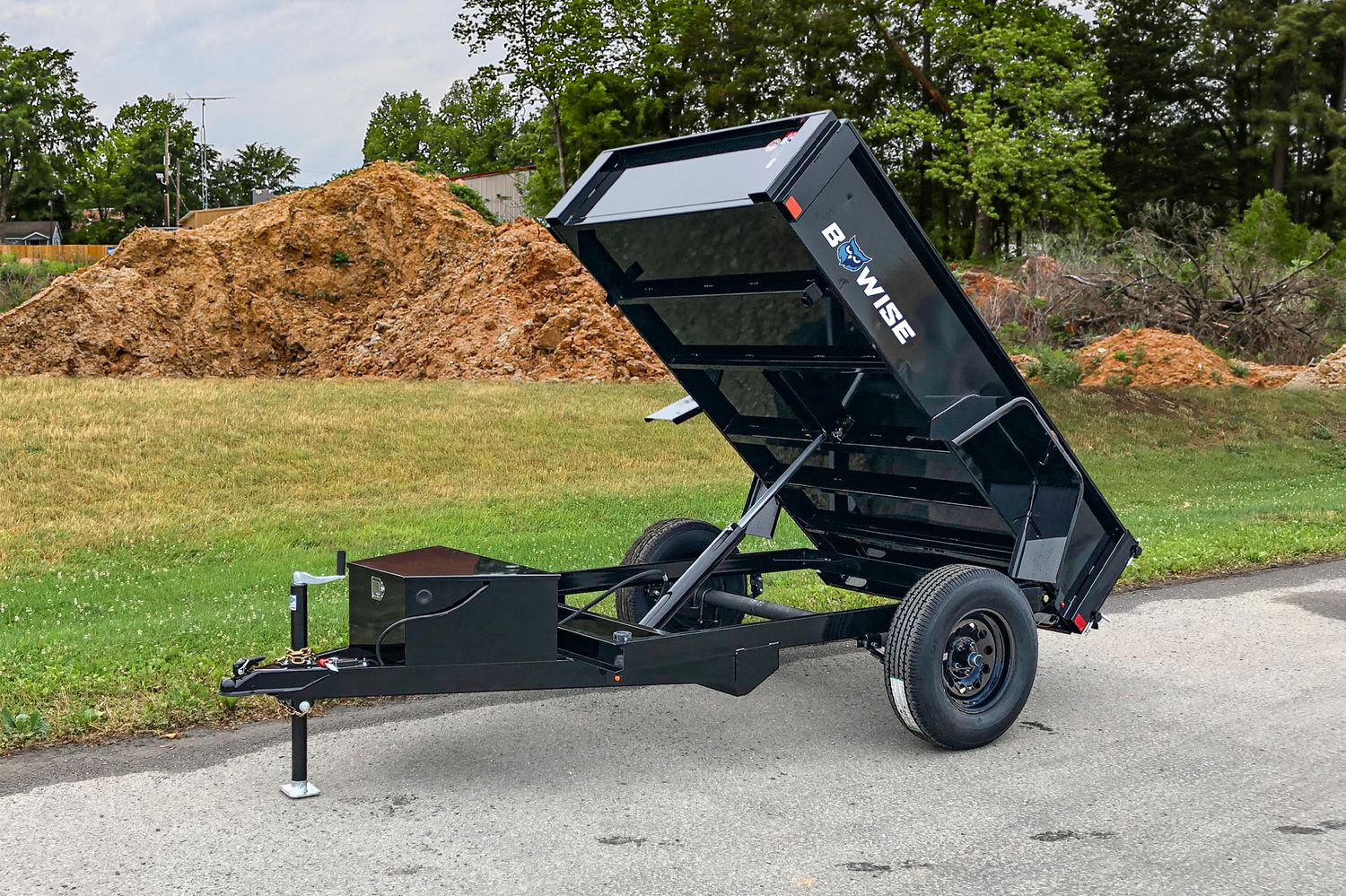 BWise Dump Trailer out in a field on top of concrete.