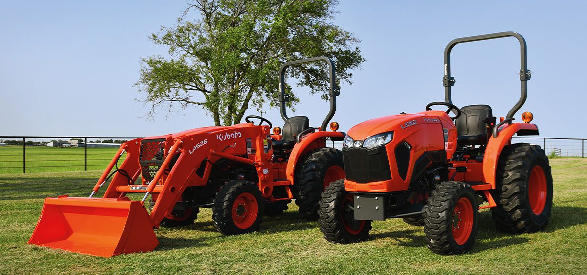 Two Kubota Standard Series Compact Tractors, one with a digging and excavation attachment, sitting in a field.