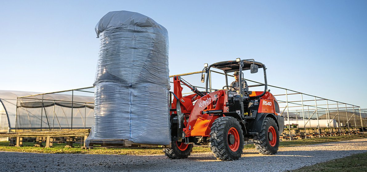 Person transporting heavy agricultural supplies using a Kubota R540 Wheel Loader.