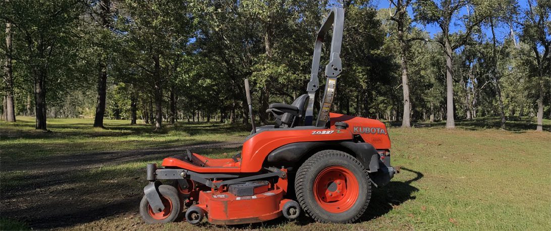 A used Kubota ZG series mower out in a field with trees in the background.