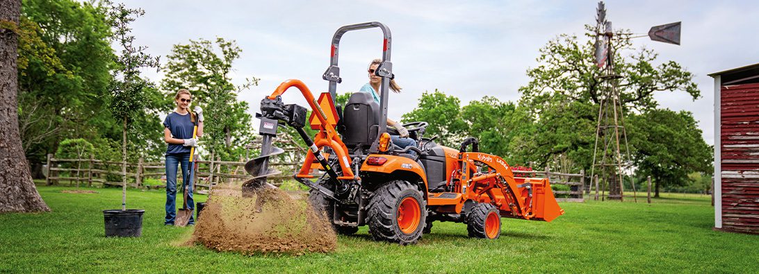 Image of Kubota tractor in a field with a Land Pride auger attachment on the back.