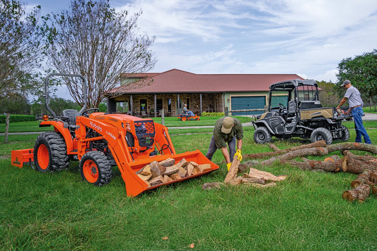 A small work crew in front of a house with various Kubota tractors and RTVs.