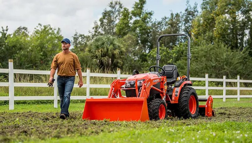Man in a pasture with a Kubota B2301HSD tractor in the background with an excavator attachment.